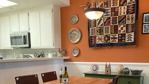 A dining area with a wooden table and chairs, a green sideboard, and a kitchen in the background. - Surf City/Sunset Beach Condo (Huntington Beach)