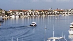 A marina with boats docked, a small boat moving across the water, and buildings in the background. - Surf City/Sunset Beach Condo (Huntington Beach)