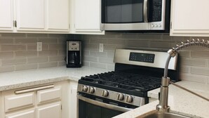 A kitchen with white cabinets, a stainless steel range, a microwave, and a coffee maker. - Surf City/Sunset Beach Condo (Huntington Beach)