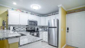 Una cocina con armarios blancos, un refrigerador de acero inoxidable, un microondas y una encimera de granito.