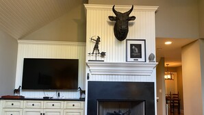 A living room with a fireplace, a mounted bull head, a framed picture, and a large flat-screen TV.