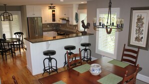 A kitchen with white cabinets, a stainless steel refrigerator, a wooden dining table with four chairs, and a chandelier.