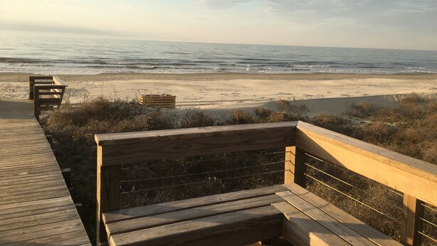 A wooden bench overlooking a beach with a wooden boardwalk leading to it.