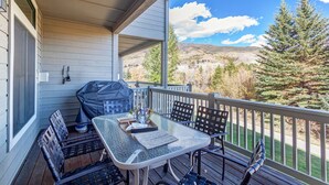 Une terrasse extérieure couverte, équipée d’une table et de chaises, d’un barbecue, et offrant une vue panoramique sur un paysage montagneux.