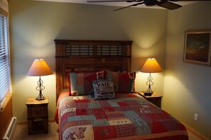 A bedroom with a wooden headboard, two bedside tables with lamps, a quilted bedspread, and a ceiling fan. - Riverside Mountain View Townhome (Silverthorne)