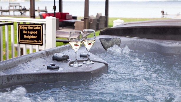 A hot tub with two glasses of white wine, a wooden gazebo, and a sign that reads "Enjoy the Lake Be a good Neighbor."