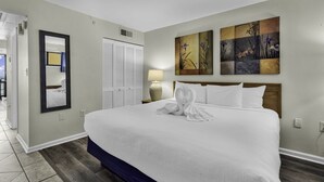 Una habitación de hotel con una cama grande, un espejo, una puerta y un cuadro en la pared.
