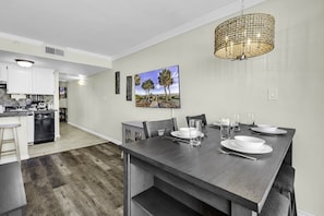 A modern kitchen with white cabinets, a dark wooden dining table set for four, and a large painting of palm trees on the wall.