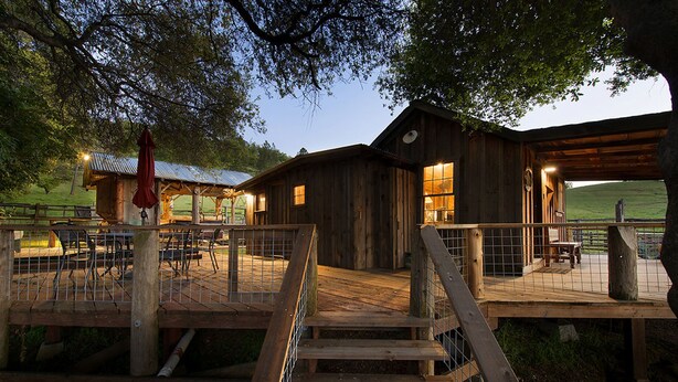 Un bâtiment rustique en bois, doté d’un espace extérieur couvert avec des sièges et d’un escalier menant à une terrasse.