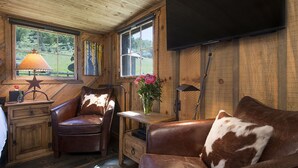 L’intérieur chaleureux d’un chalet avec un canapé en cuir, un meuble en bois, une lampe et un téléviseur fixé au mur.