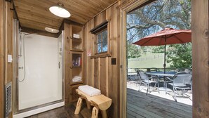 Une cabane en bois avec une douche, un banc et une table avec des chaises à l’extérieur.
