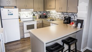 A modern kitchen with beige cabinets, a white refrigerator, a microwave, a stove, and a large island with two stools. - 🌄Resort Vacations at Fairfield Glade TN Two bedroom villa (Fairfield Glade)