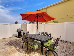 An outdoor patio with a metal table and chairs, a red umbrella, and a barbecue grill.