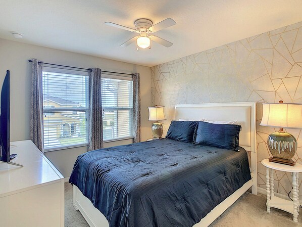 A bedroom with a bed, two bedside tables with lamps, a ceiling fan, and a window with blinds.