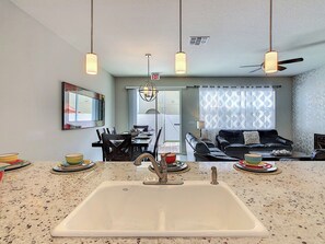 A modern kitchen with a central island, pendant lighting, and a ceiling fan.