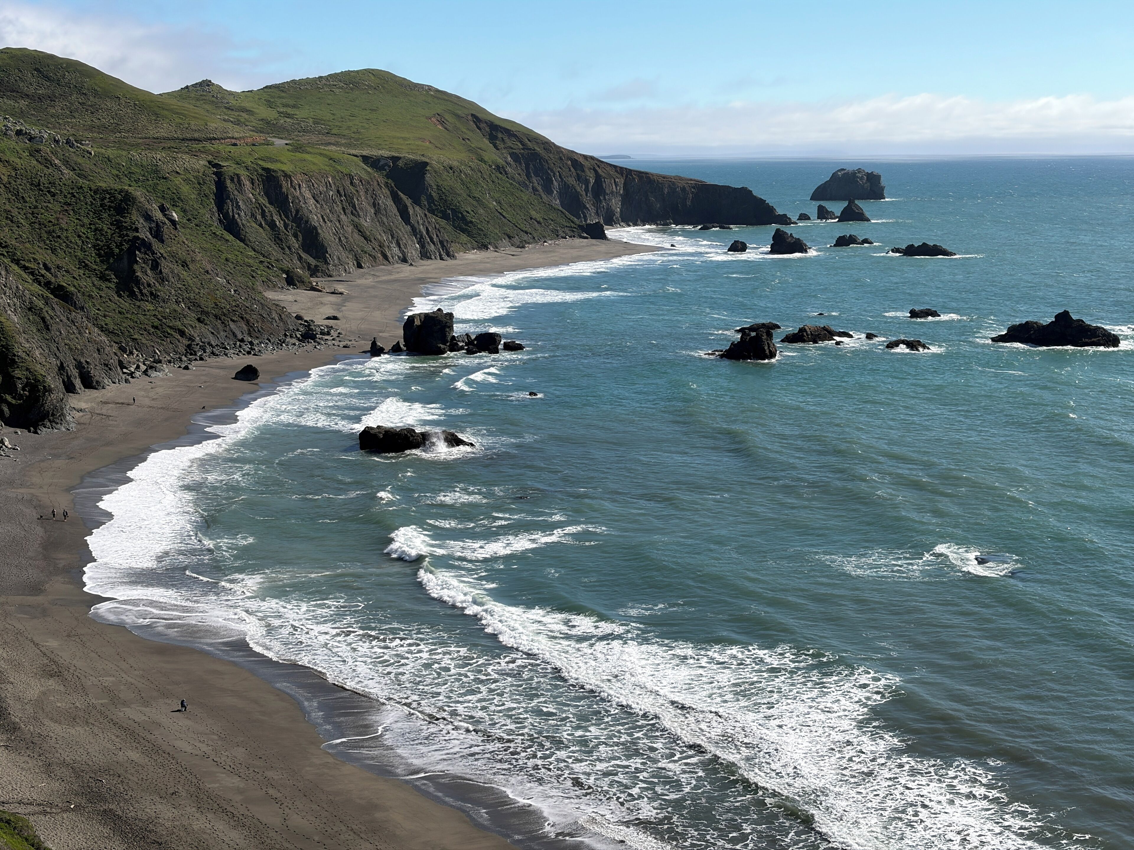 Un paysage côtier caractérisé par une plage de sable, des affleurements rocheux et des collines verdoyantes.