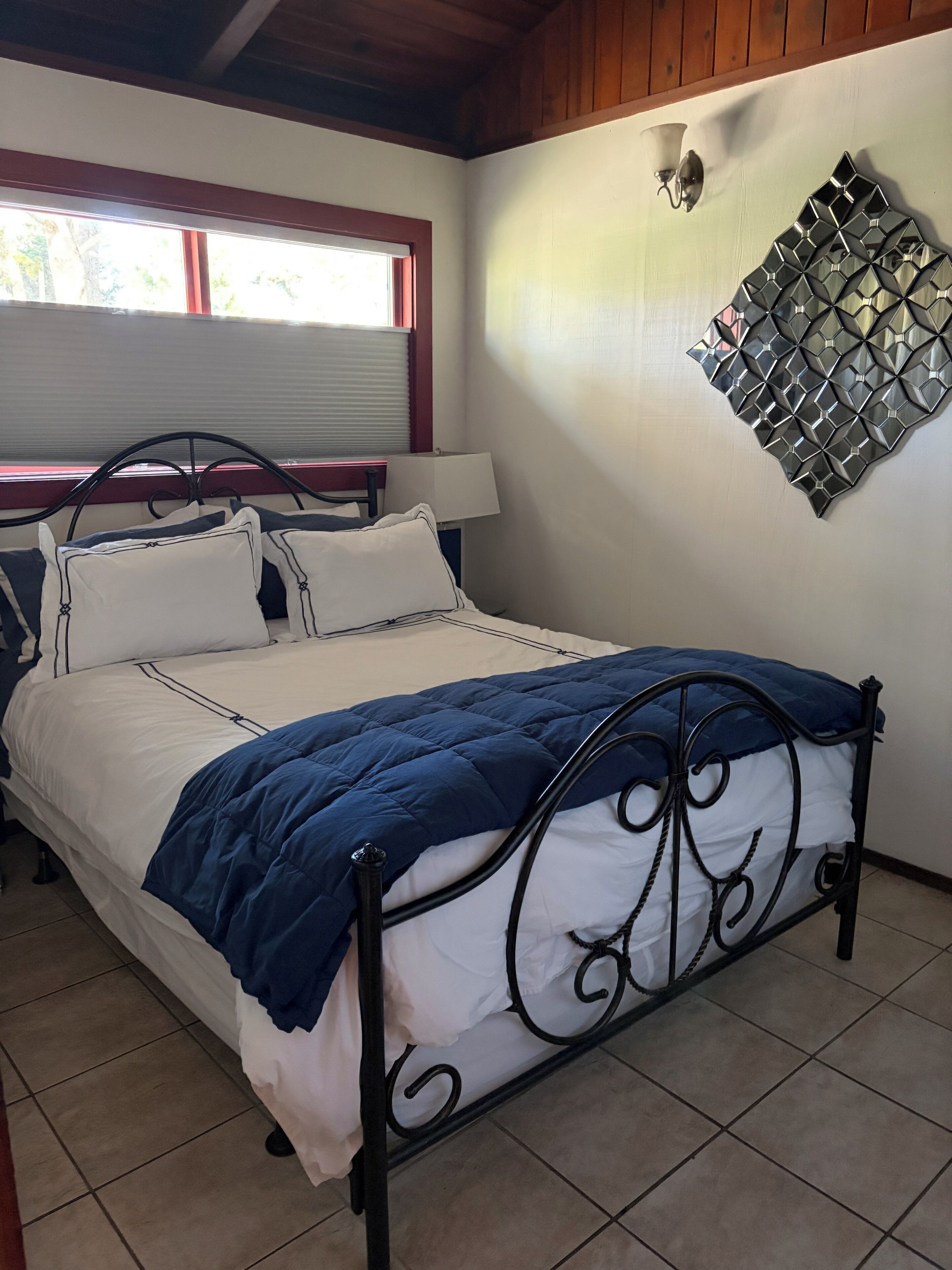 Una cama con estructura de metal, ropa de cama blanca y una manta azul.