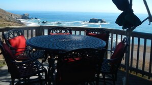 Une table ronde en métal, des chaises, une vue sur l’océan et des falaises rocheuses.