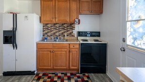 A compact kitchen with wooden cabinets, a refrigerator, a stove, and a tiled backsplash. - Hippohead Casita Pets stay free bring your Humans! (Homosassa)