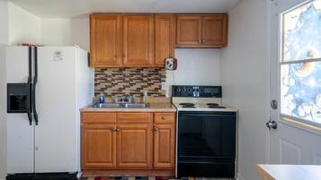 A compact kitchen with wooden cabinets, a refrigerator, a stove, and a tiled backsplash.