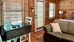 Interior de una cabaña de madera con una mesa de comedor, un sofá y una puerta con ventana.
