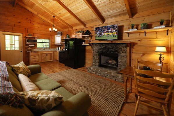 Un interior de cabaña acogedor, con chimenea de piedra, muebles de madera y un televisor montado encima.