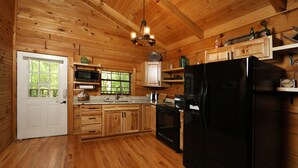 Cocina de cabaña de madera con un refrigerador negro, armarios de madera, un microondas y una lámpara colgante.