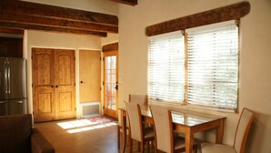A dining area with a wooden table and chairs, a kitchen with a refrigerator, and a wooden door.