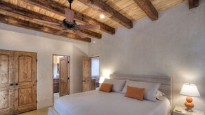 A bedroom with a large bed, wooden wardrobe, ceiling fan, and bedside lamp.
