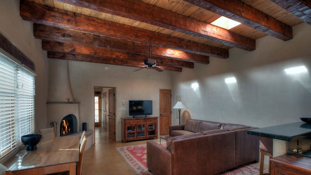 A living room with a wooden ceiling, a television, a fireplace, a sofa, and a dining table with chairs.
