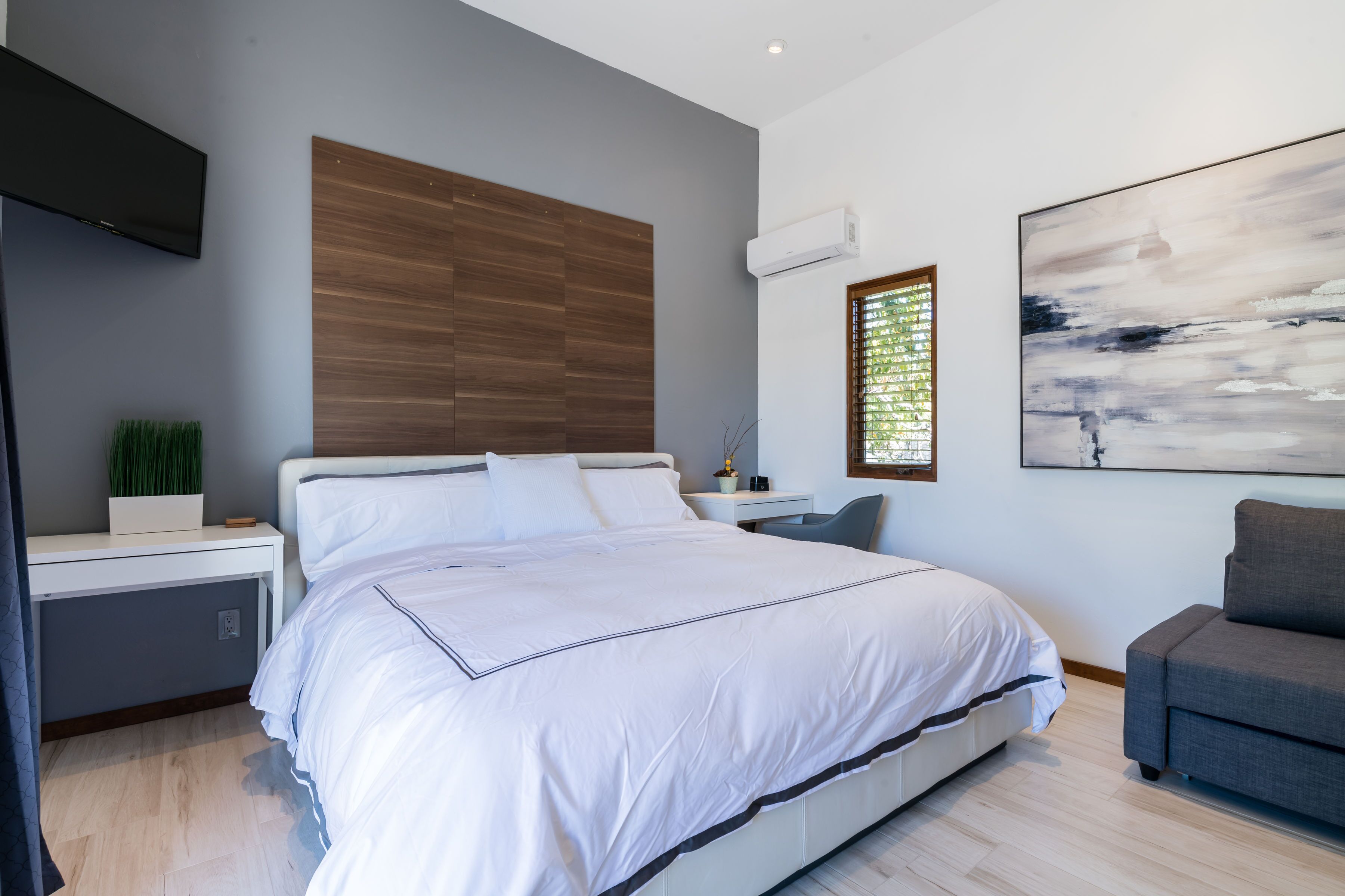 Une chambre à coucher moderne avec un grand lit, un bureau, un canapé gris et un tableau au mur.