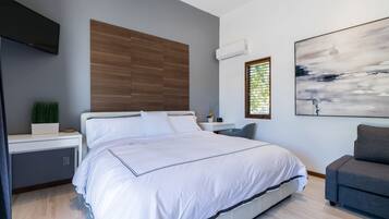 Une chambre à coucher moderne avec un grand lit, un bureau, un canapé gris et un tableau au mur.
