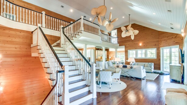 A spacious living area with a wooden staircase, a round coffee table, and a sofa. - 24 Dene Court Beautiful  8 Bedroom Home in DeBordieu, Private Pool! (Georgetown)