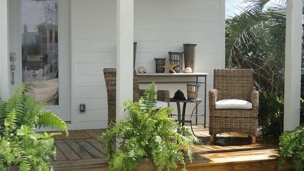 Una terraza de madera con mobiliario de mimbre y plantas en macetas.