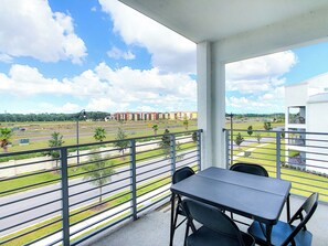 A balcony with a table and chairs, overlooking a road and buildings.