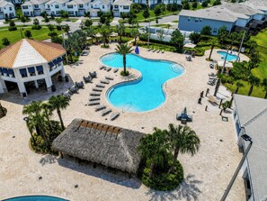 A resort with a central swimming pool, lounge areas, and a thatched-roof structure.
