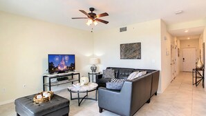 A living room with a television, sofa, ottoman, and a ceiling fan. - Family Fun: Condo near Theme Parks & Pools! (Kissimmee)