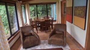 Un comedor con una mesa redonda y sillas, ventanas amplias y dos sillones de cuero.