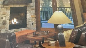 A cozy living room with a stone fireplace, leather sofa, and a round wooden table with a lamp.