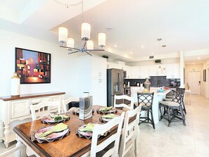 A modern kitchen with white cabinets, a central island, and a dining area with a wooden table and chairs. - Kissimmee Condo: Pools, parks, family fun, and attractions! (Kissimmee)