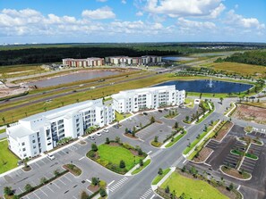 A multi-story hotel with a parking lot and a landscaped area with a pond.