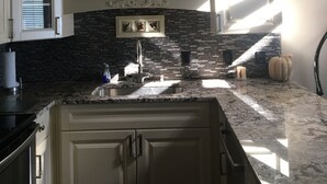 A kitchen with white cabinets, a black backsplash, and a granite countertop.