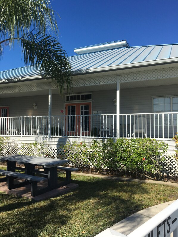 A building with a covered porch, a red door, and a white fence.