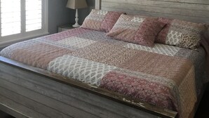 A bedroom with a bed, a ceiling fan, a wall sign saying "Welcome to Our Home," and a nightstand with a lamp.