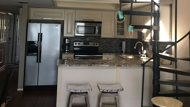 A kitchen with a central island, stainless steel appliances, and a black spiral staircase.