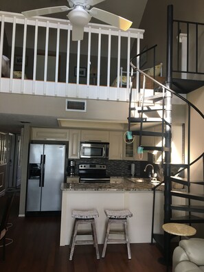 Una cocina con isla central, electrodomésticos de acero inoxidable y una escalera espiral negra.