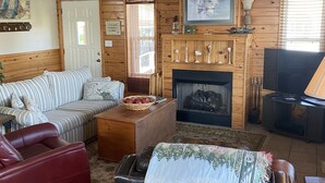 Ein gemütliches Wohnzimmer mit einer Holzwand, einem Sofa, einem roten Sessel, einem Couchtisch und einem Kamin.