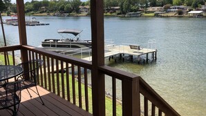 Eine Holzterrasse mit Tisch und Stühlen, mit Blick auf einen ruhigen See, im Hintergrund Boote und Häuser.