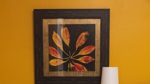 Une commode en bois foncé, dotée de nombreux tiroirs, est placée contre un mur jaune. Au-dessus, on aperçoit une œuvre d’art encadrée, et une lampe de table blanche est posée sur le dessus.