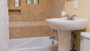 Une salle de bain avec une baignoire, un lavabo et des toilettes. On y trouve des articles de toilette accrochés au mur et un pommeau de douche.